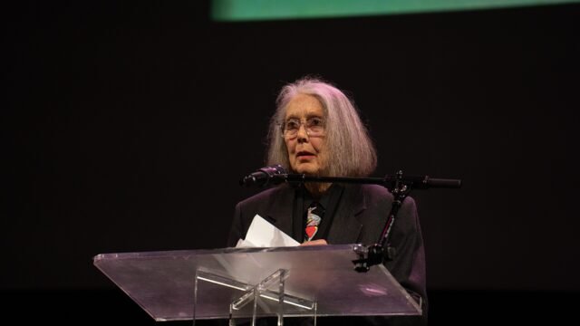 Anne Carson reading at a lectern on stage