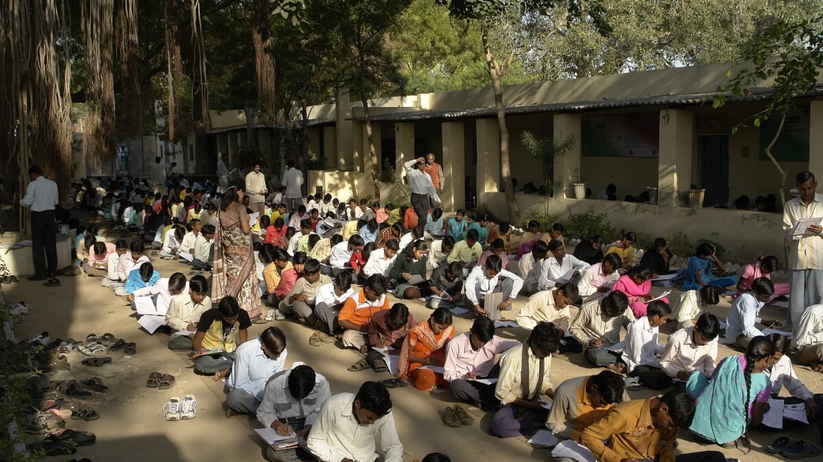 Rows of students sitting on the ground in a school compound writing an exam