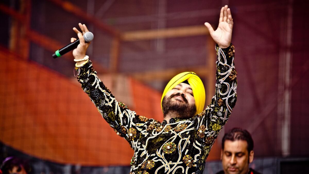 Daler Mehndi in a yellow turban raising both arms while singing on stage