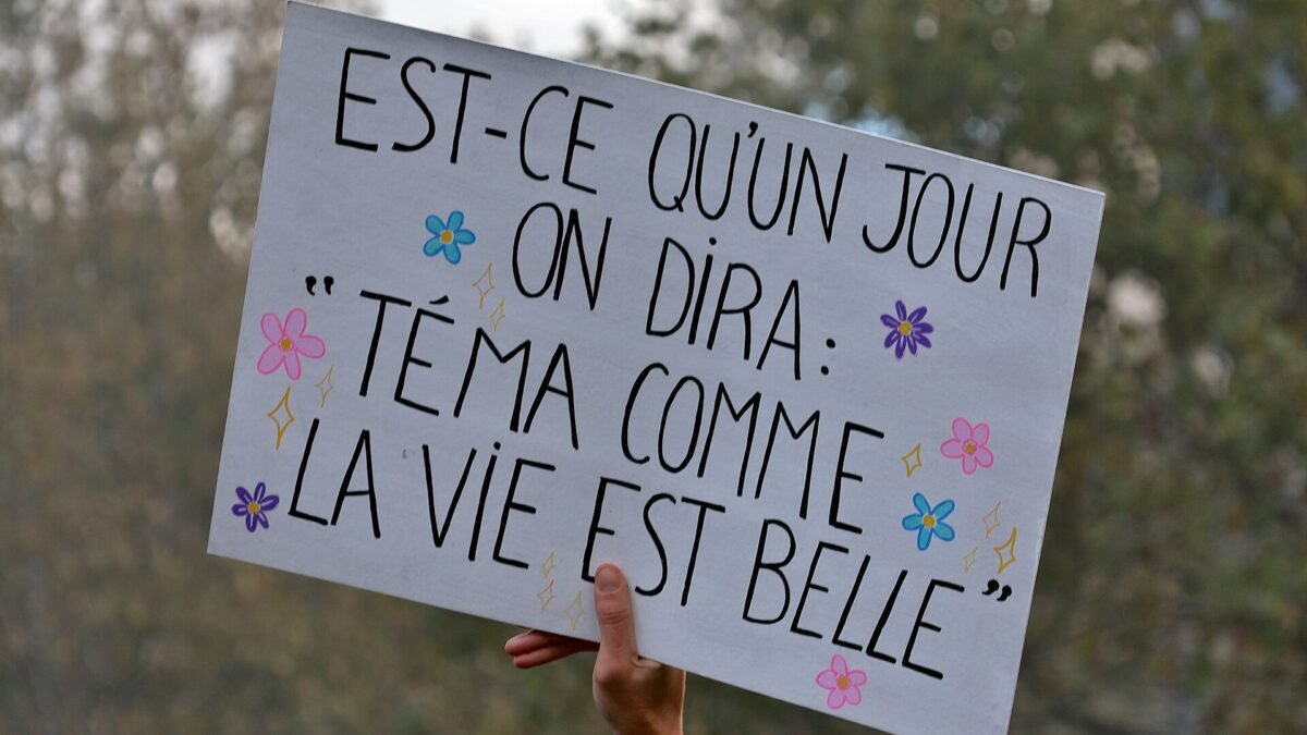 A hand holds up a white cardboard placard with French slogan and drawn flowers at a Paris protest