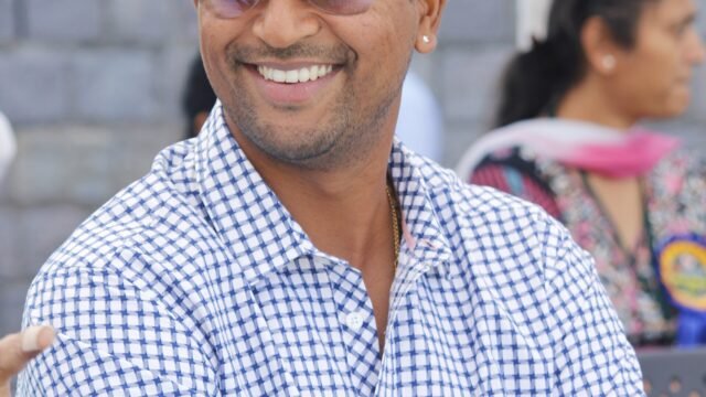 Former India spinner Pragyan Ojha smiling, arms folded, in a checked shirt and sunglasses